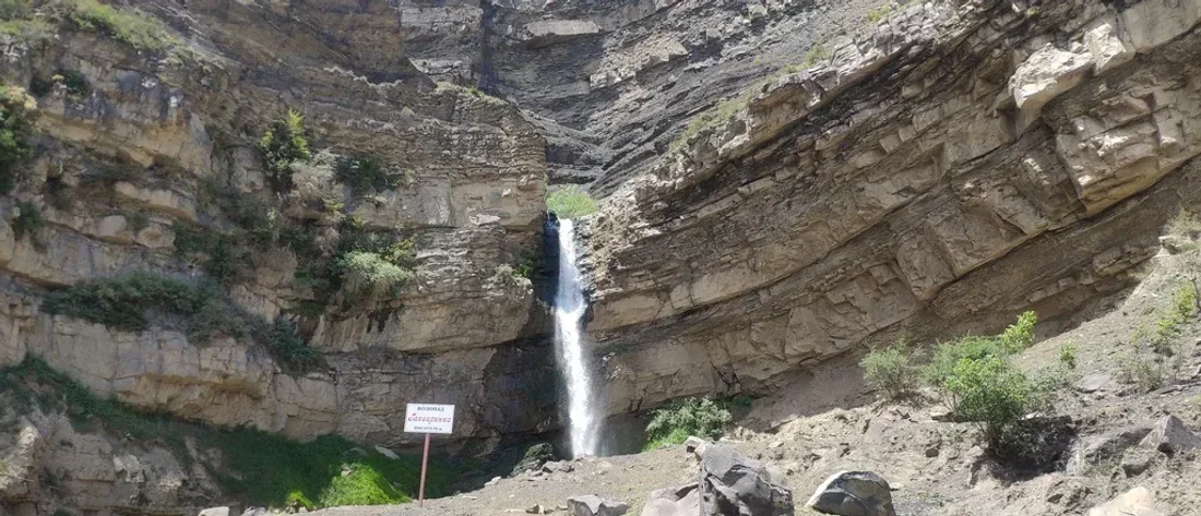 Гакваринский водопад падает в узком скальном амфитеатре, у подножия стоит табличка памятника природы