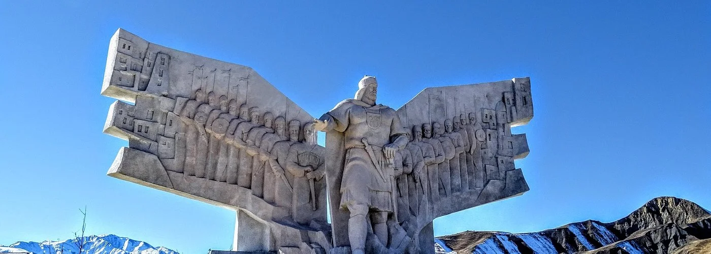Памятник хану Муртазали в Кумухе зимой: воин в центре и войско горцев на каменных крыльях по бокам, на фоне заснеженных гор